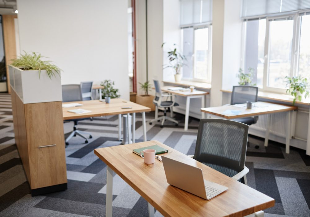 Desk with mug, planner and opened laptop in empty open space coworking center